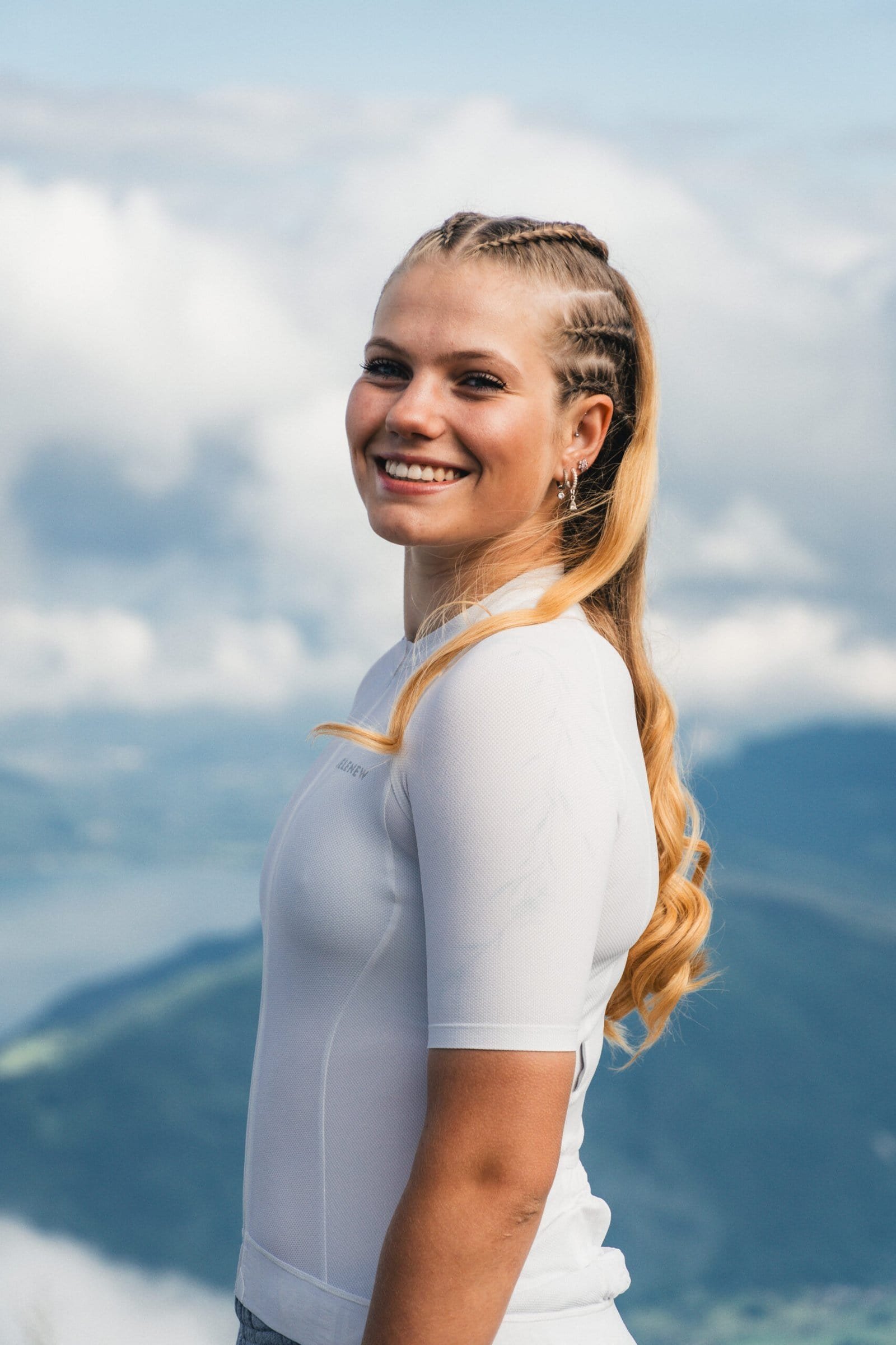 Jeune femme souriante en extérieur avec montagnes en arrière-plan.