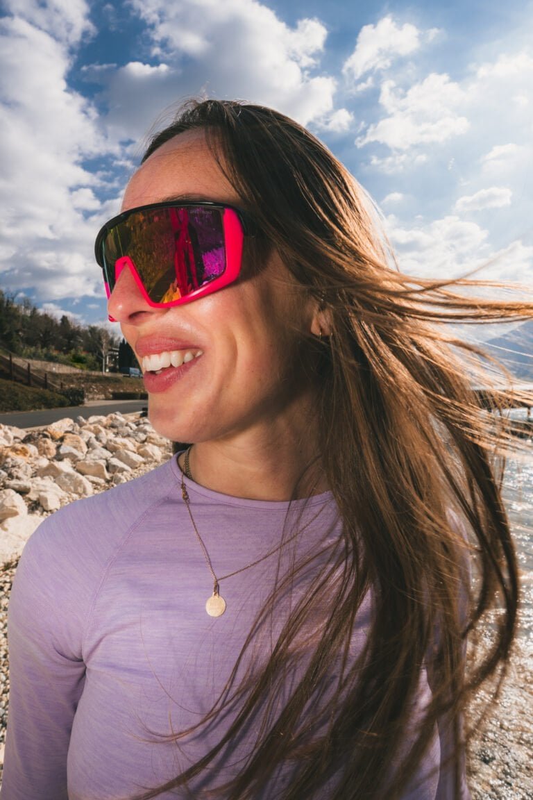 Femme souriante portant des lunettes de soleil roses en plein air.